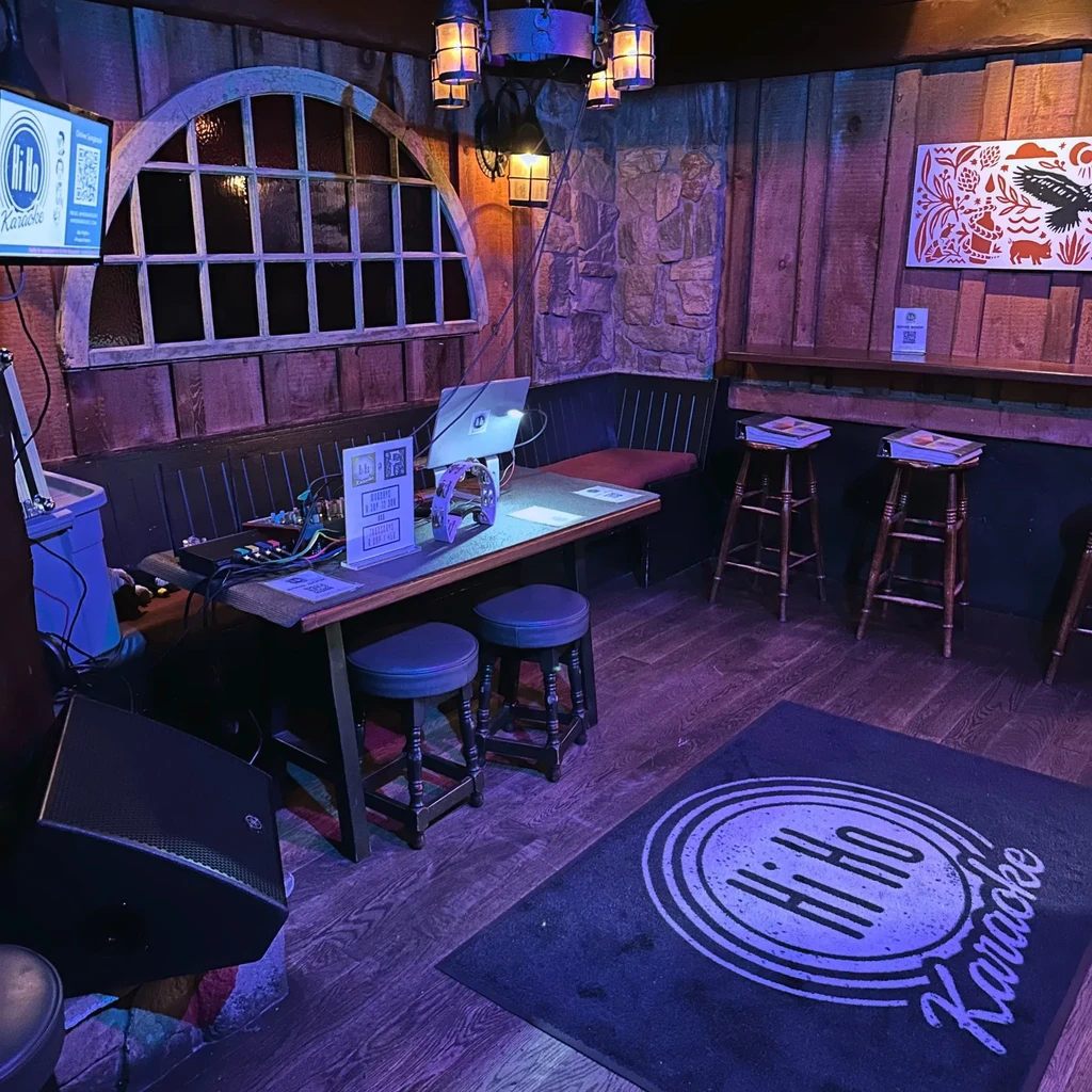 Dimly lit, rustic pub with karaoke setup and "Hi Ho Karaoke" branding.