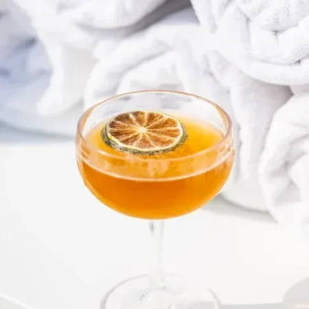 Amber cocktail in coupe glass, garnished with a dried citrus wheel.
