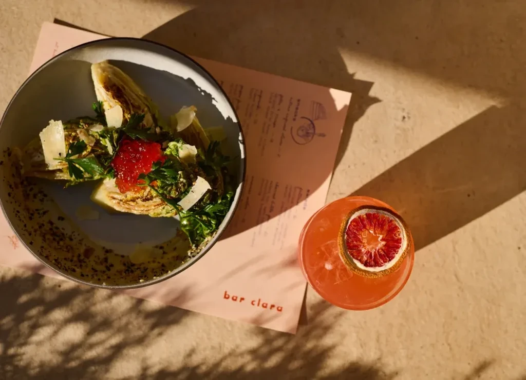 Top-down: salad with roe, orange cocktail, and "bar clara" paper.