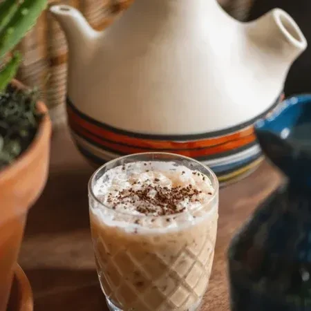 Frothy beige drink in a clear, diamond-patterned glass with sprinkles.