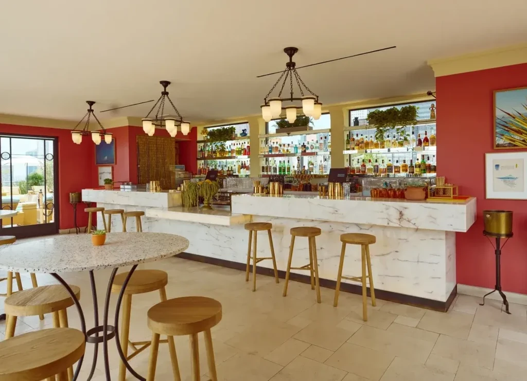 Empty modern bar with white marble counter, backlit liquor, and red walls.