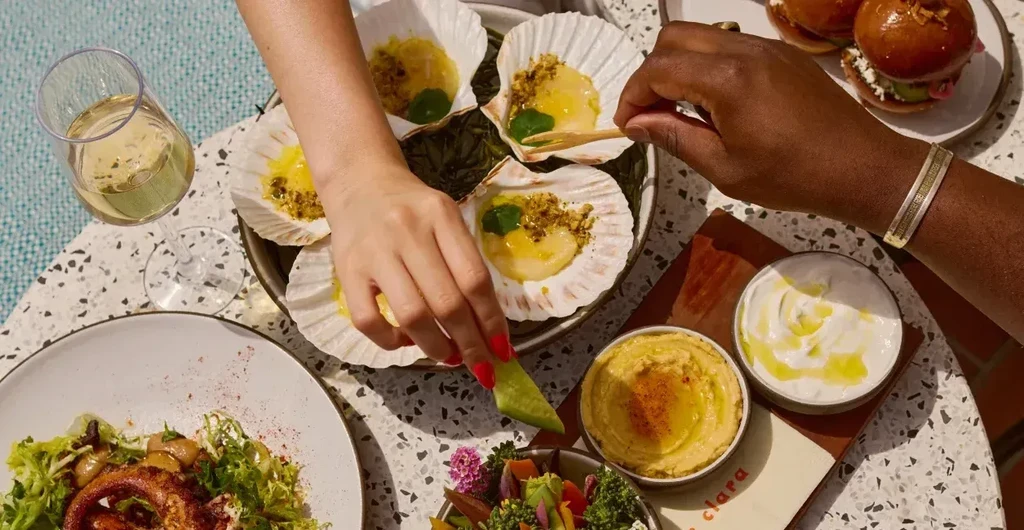 Two hands reach for gourmet scallops and octopus on a bright table.