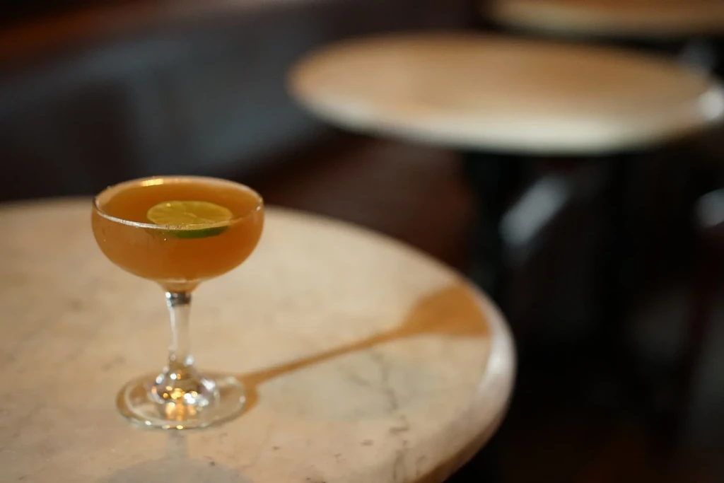 Single amber cocktail in coupe glass with lime, blurred background.