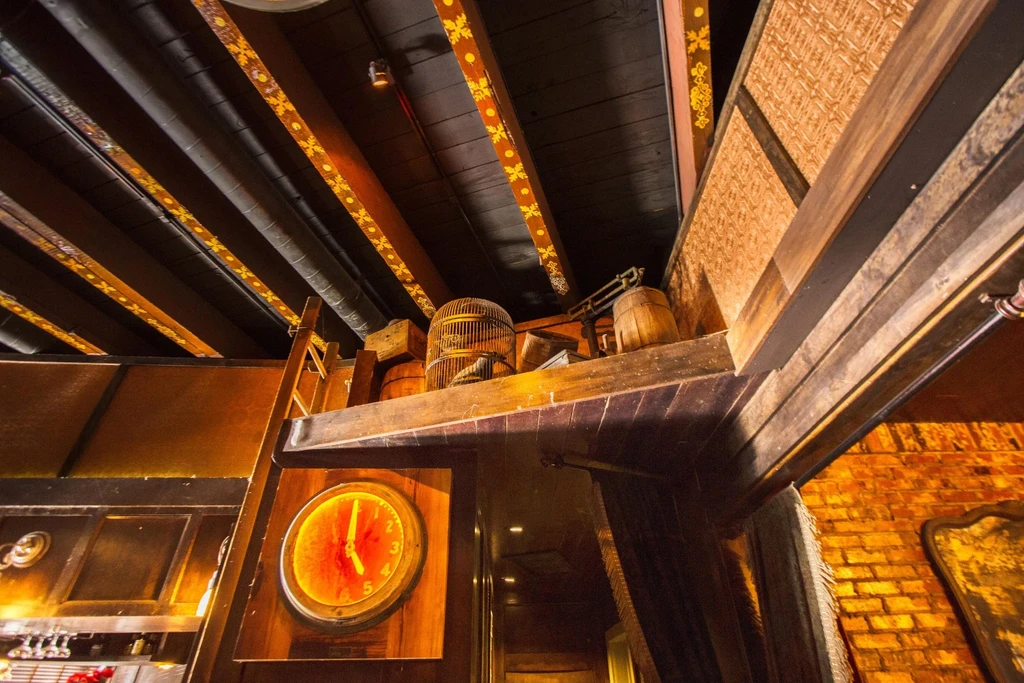 Rustic restaurant interior with ornate wooden beams, elevated shelf, and glowing clock.