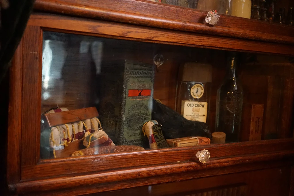 Dark wooden display cabinet showcases vintage bottles, pouches, and a corncob.