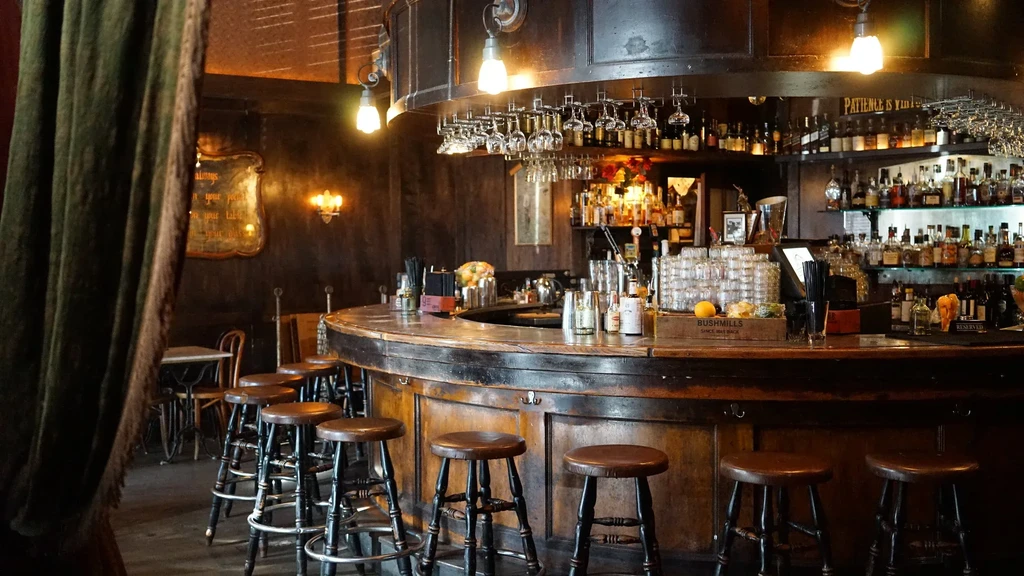Warmly lit classic wooden bar with liquor bottles and stools.