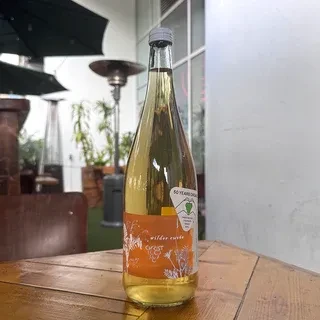 Organic white wine bottle on a wooden table in an outdoor setting.