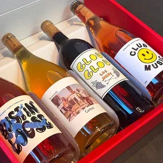 Four uniquely labeled wine bottles, varied colors, in a red box.