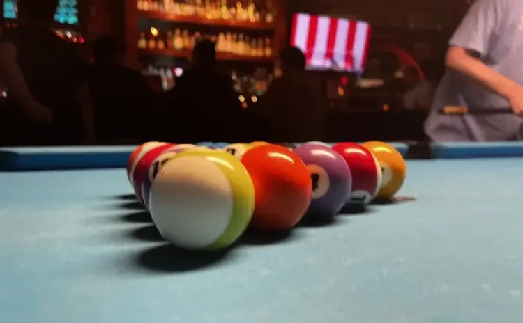 Racked colorful pool balls on a blue table, bar background.