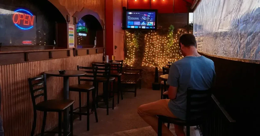 Evening restaurant patio with string lights, television, and neon 'OPEN' sign.