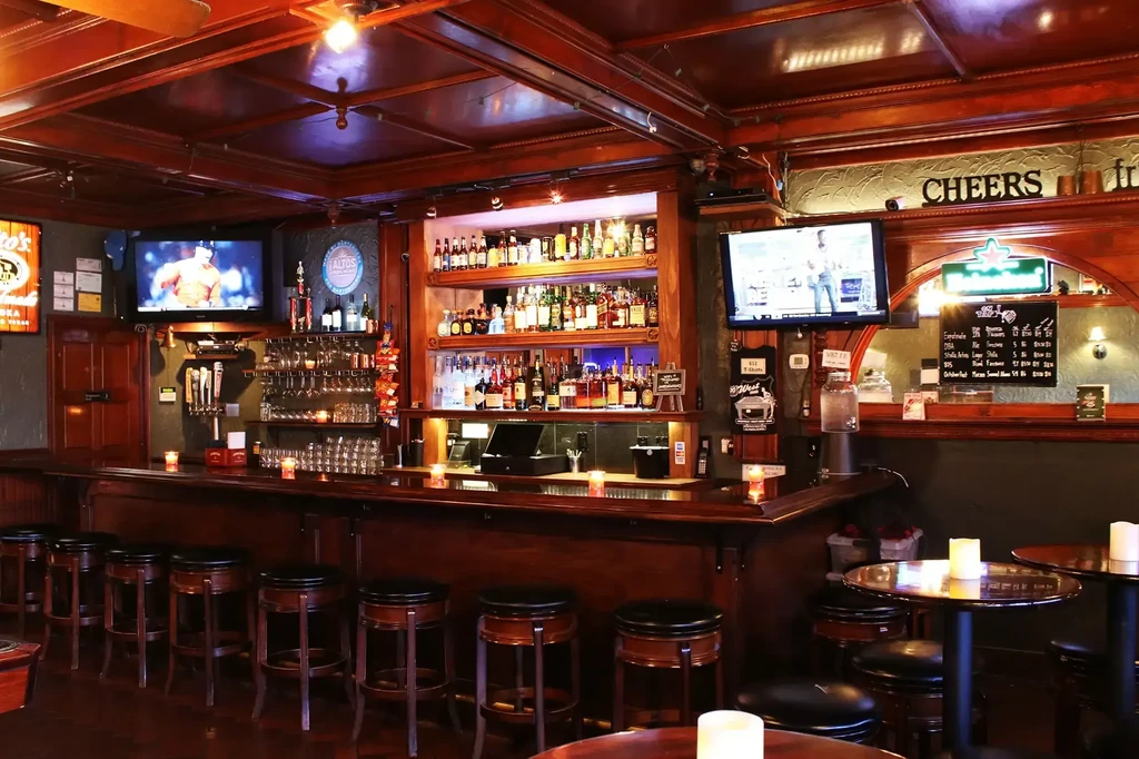 Warmly lit pub interior, long dark wooden bar, stocked liquor shelves.