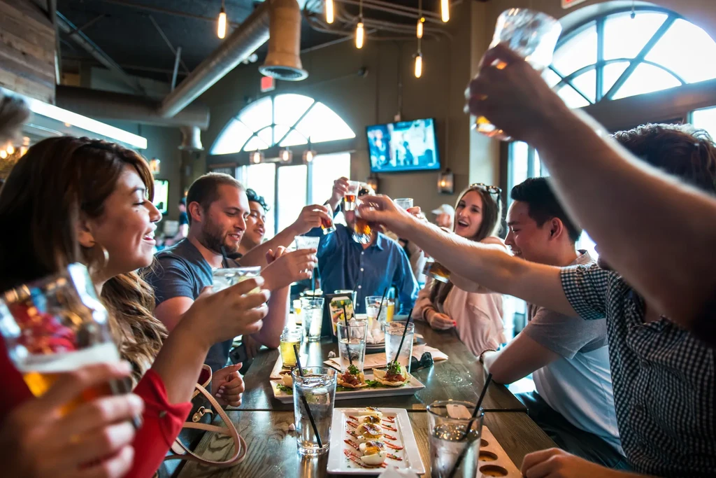 Smiling young adults toast with drinks and food in a modern restaurant.