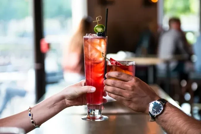Two hands raise distinct red and amber cocktails in a toast.