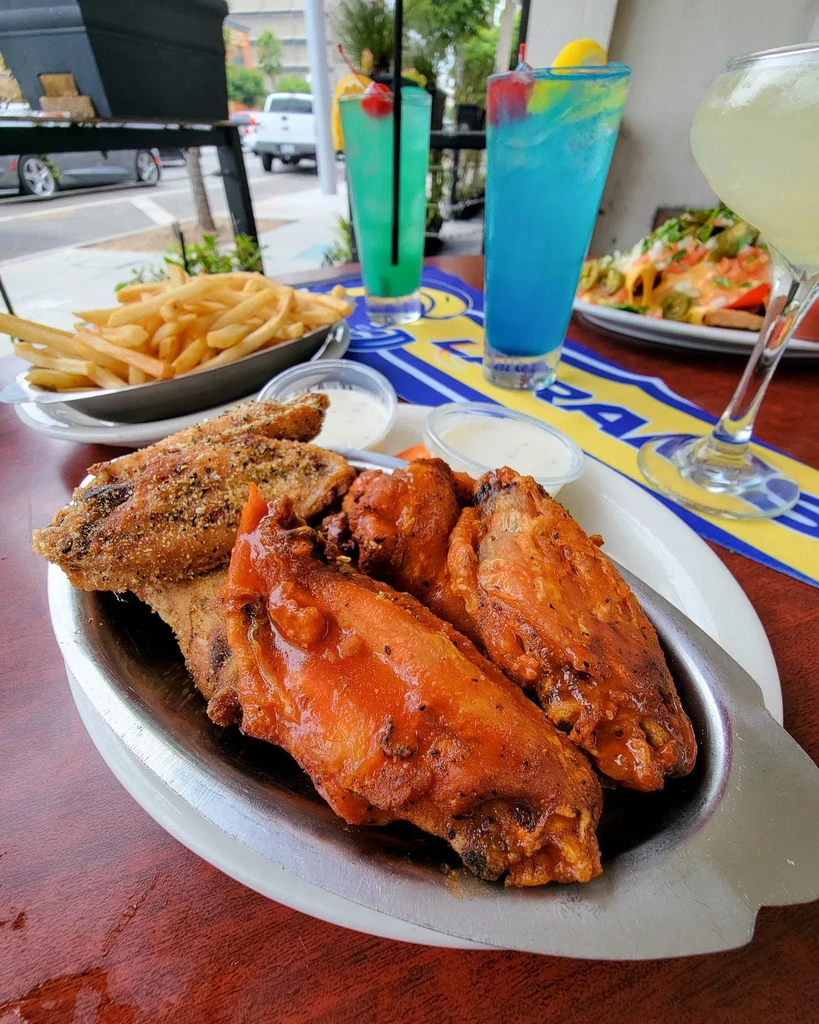 Chicken wings, fries, nachos, and colorful cocktails on an outdoor table.