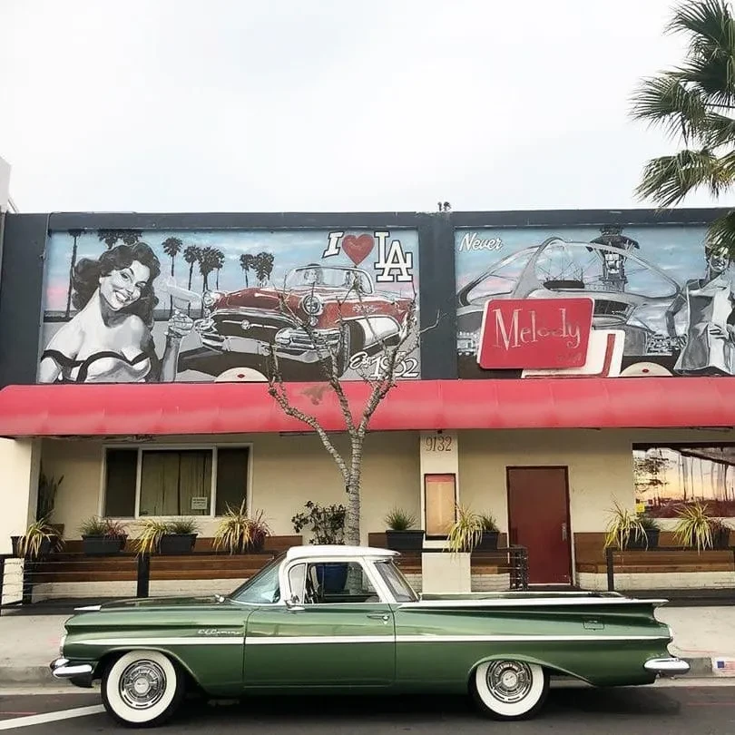 Retro building with 'I ❤️ LA' mural and vintage Chevrolet El Camino.
