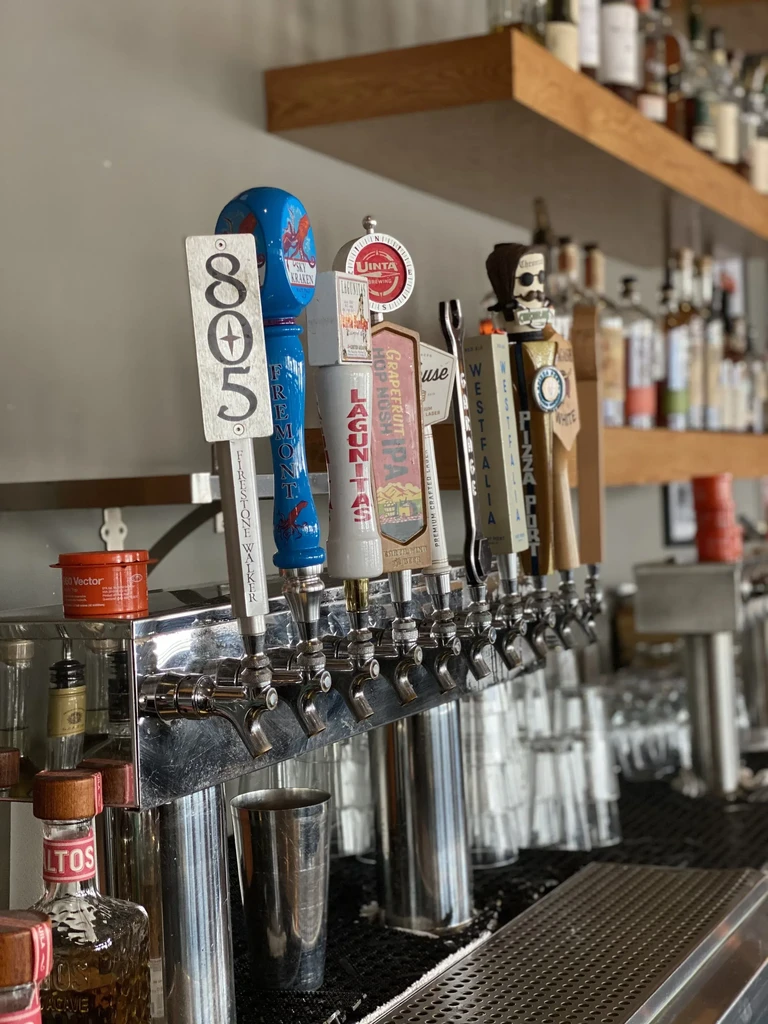 Eight unique, branded beer tap handles at a well-stocked bar.