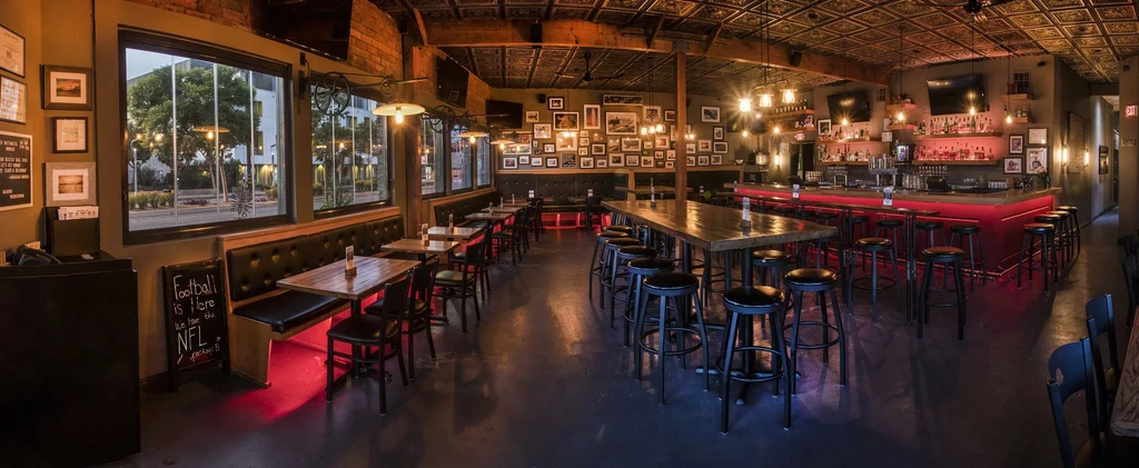 Empty modern rustic bar interior with diverse seating and red-lit bar.