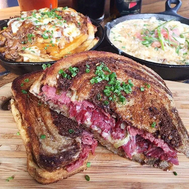 Grilled sandwich, loaded fries, and creamy skillet dish on a table.
