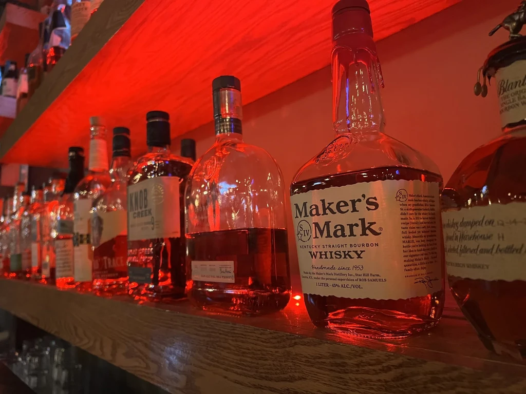 Maker's Mark and other whiskey bottles on a red-lit bar shelf.