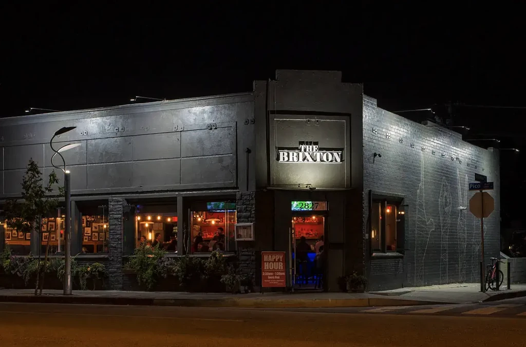 Modern The Brixton restaurant exterior at night, with illuminated sign and patrons.