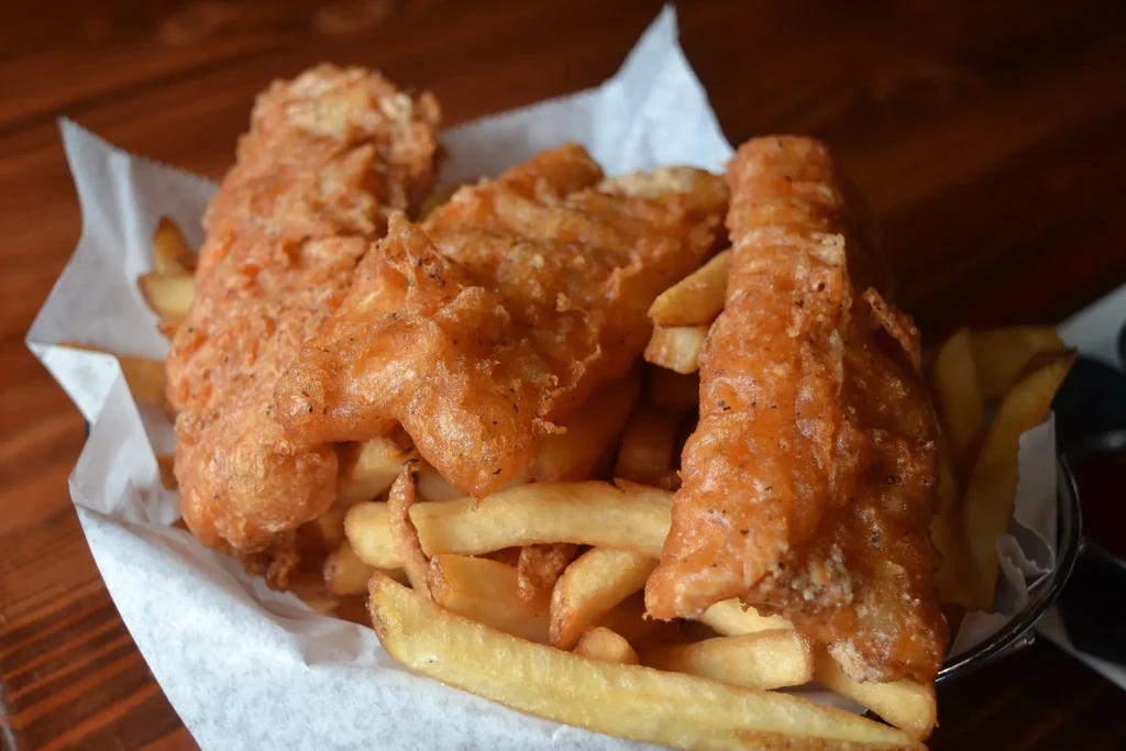 Golden-brown battered fish and chips in a basket on a wooden table.