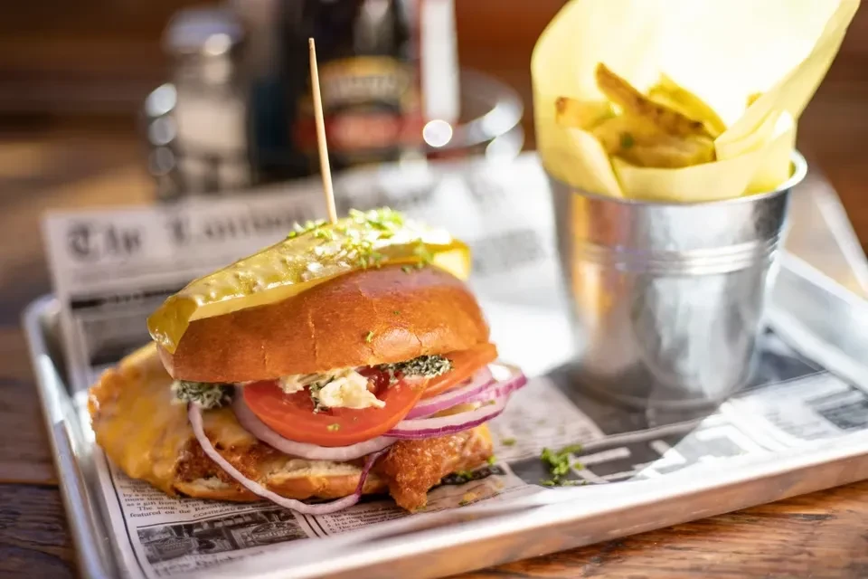 A gourmet fried chicken sandwich with fries on a newspaper-lined tray.