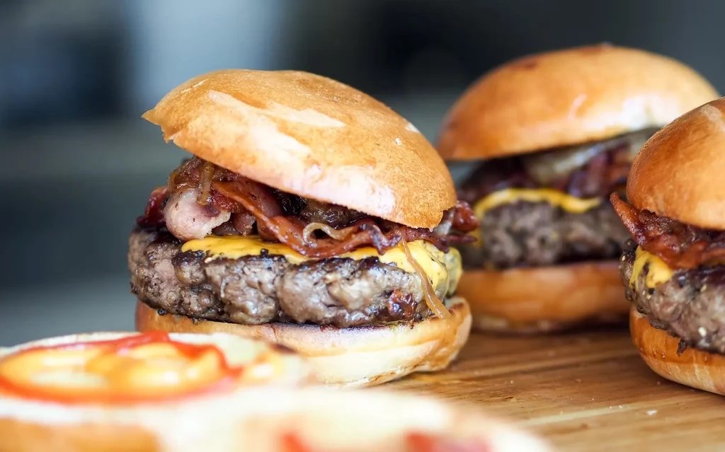 Three gourmet burgers with bacon, cheese, and onions on a wooden board.