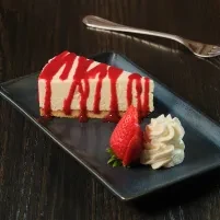 Slice of cheesecake with red fruit sauce, strawberry, and whipped cream.