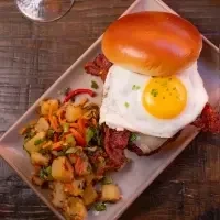Overhead: breakfast sandwich with fried egg, bacon, and roasted potatoes.