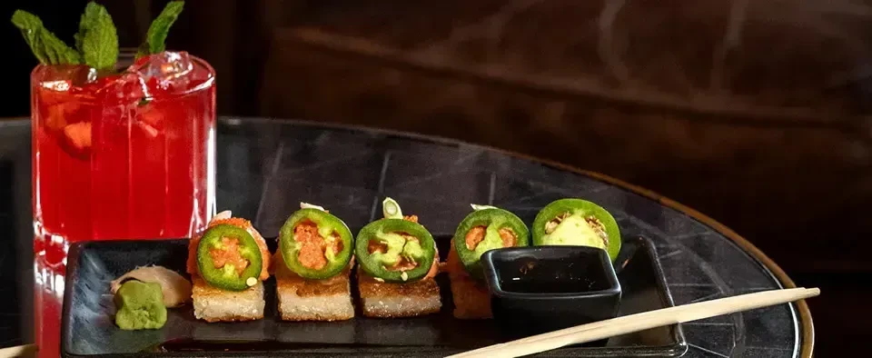 Red cocktail, square jalapeño appetizers, wasabi, pickled ginger, and chopsticks.