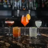 Five distinct cocktails on a dark bar, blurred background.