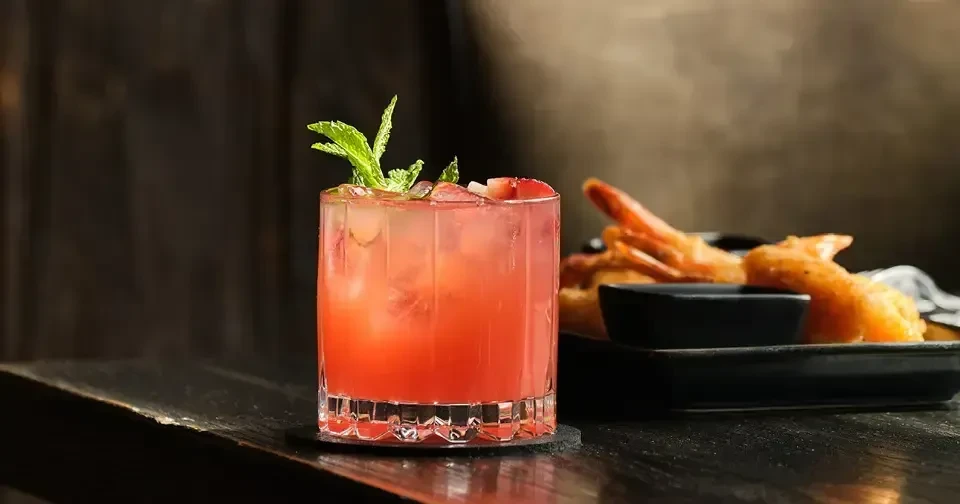 Red fruit cocktail with mint and fruit garnish, blurred appetizers.