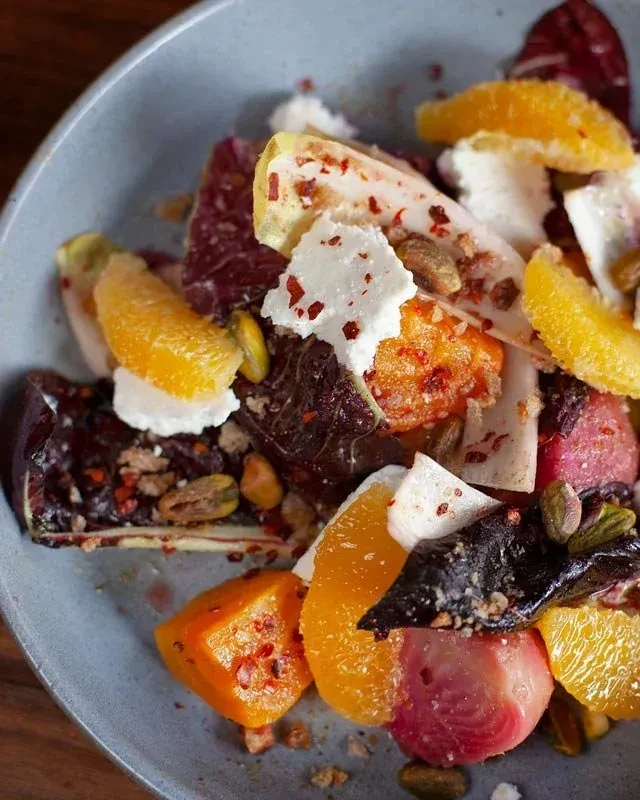 Vibrant overhead salad with citrus, radicchio, cheese, and pistachios.