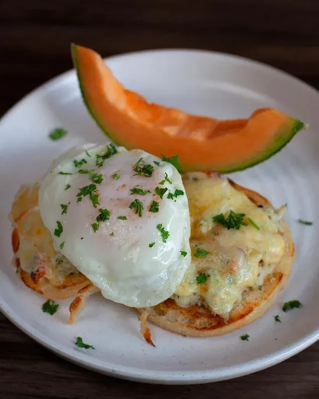 Poached egg and melted cheese on toast, with herbs and cantaloupe.