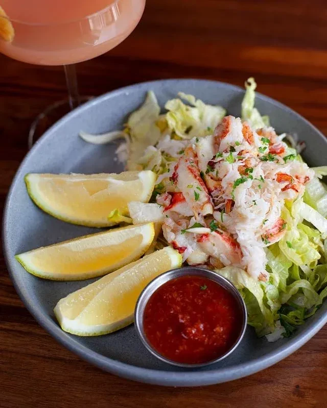 Overhead: Seafood salad, lemon wedges, red sauce, and pink drink.