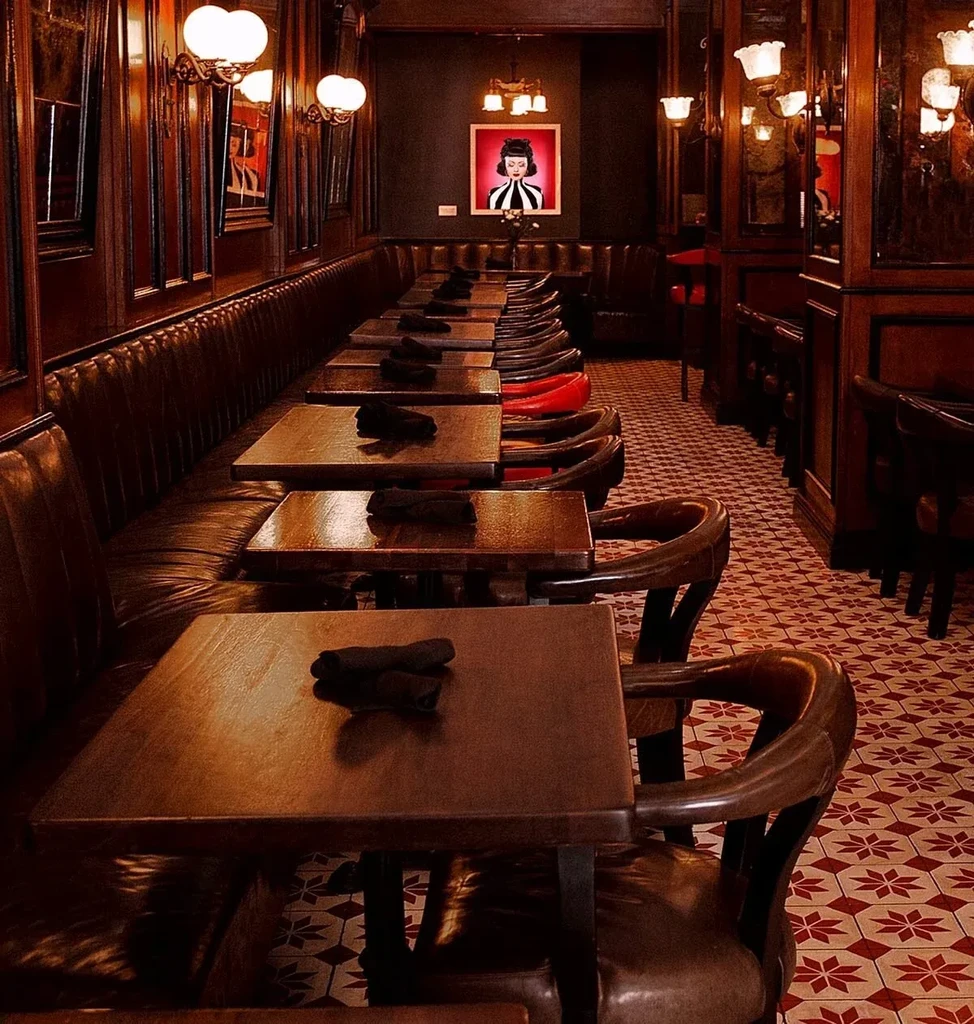 Empty dining room with dark wood panels, tufted leather booths, patterned floor.