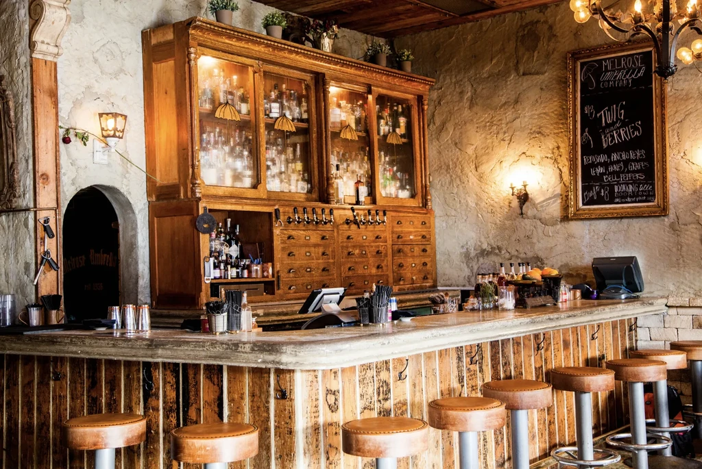 Rustic bar with well-stocked cabinet, beer taps, chalkboard menu, stools.