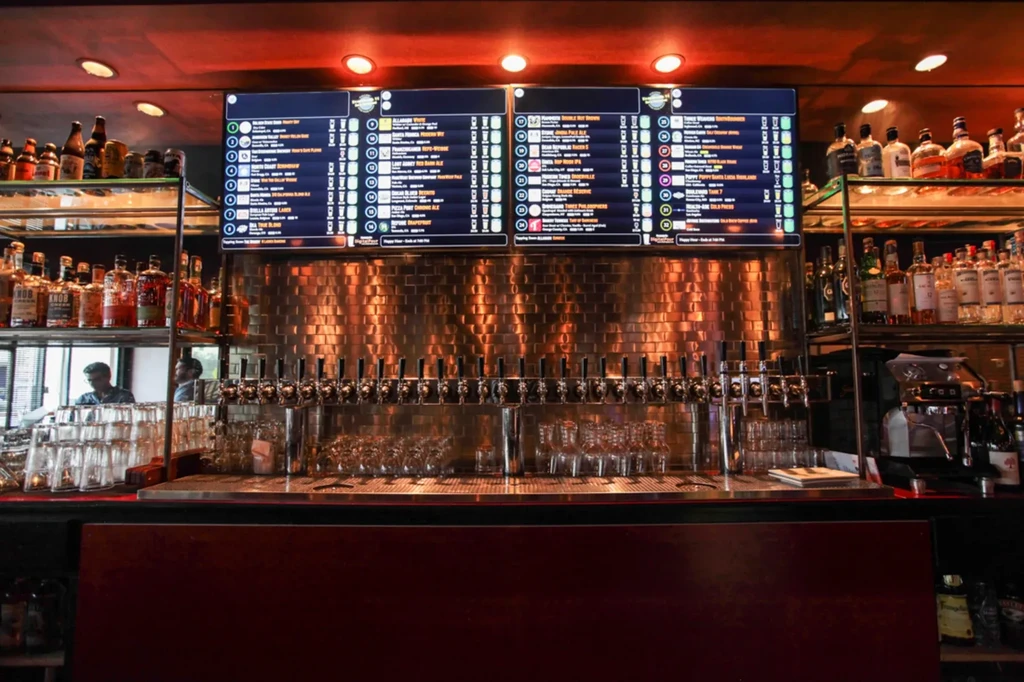 Modern bar interior with 20+ beer taps, digital menu, liquor bottles.