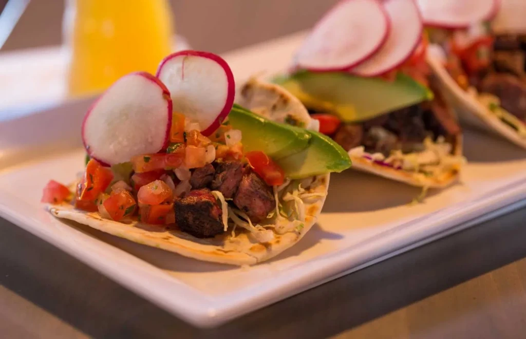 Three tacos topped with meat, cabbage, pico de gallo on a plate.