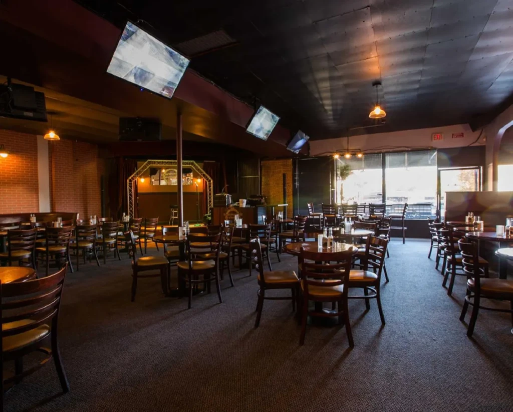Industrial-style restaurant interior with dark furniture, stage, and TVs.