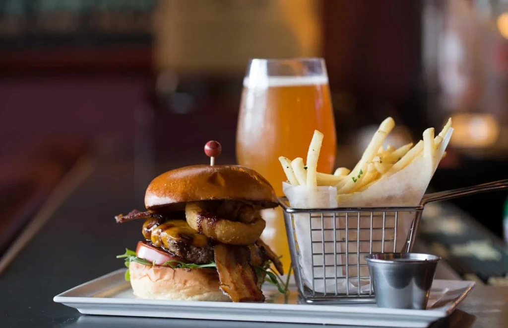 A burger with bacon and onion rings, golden fries, and beer.