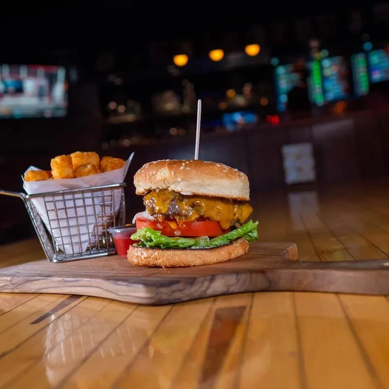 Gourmet cheeseburger and tater tots on a rustic wooden board.