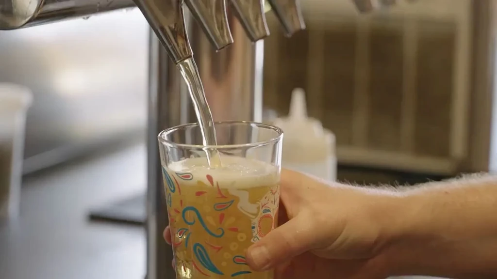 Yellowish beverage pours from dispenser into a colorful patterned glass.