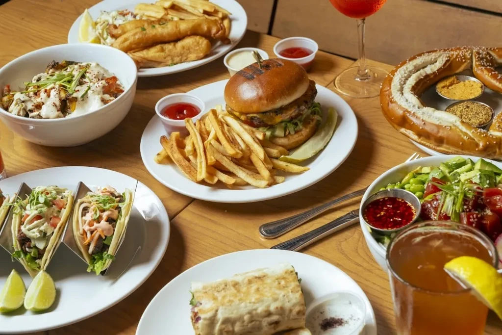 Overhead: wooden table with fish and chips, burger, tacos, pretzel, drinks.