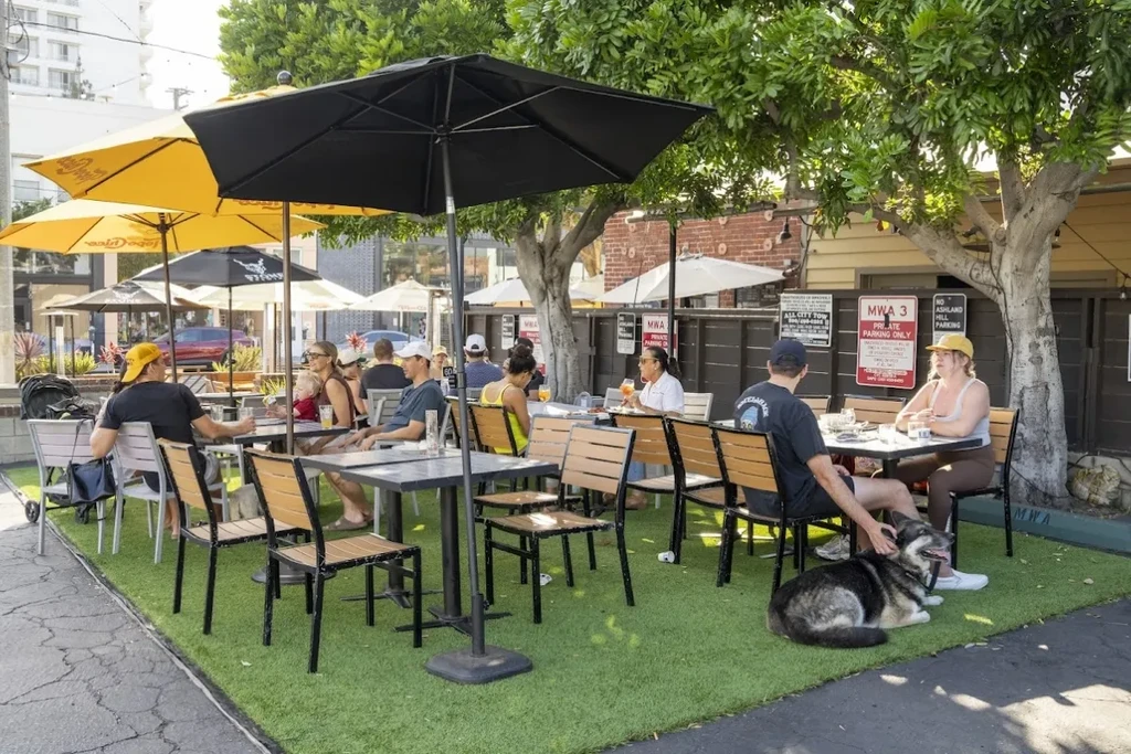 People enjoy a sunny outdoor patio with artificial turf and umbrellas.