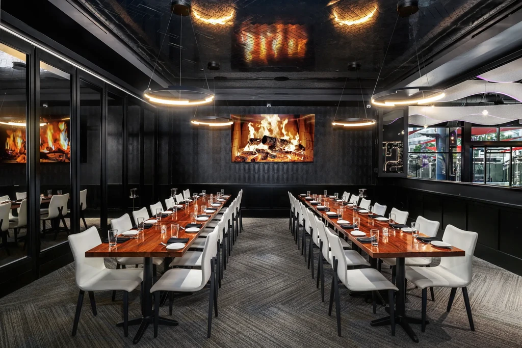 Modern private dining room with two tables, dark walls, digital fireplace.