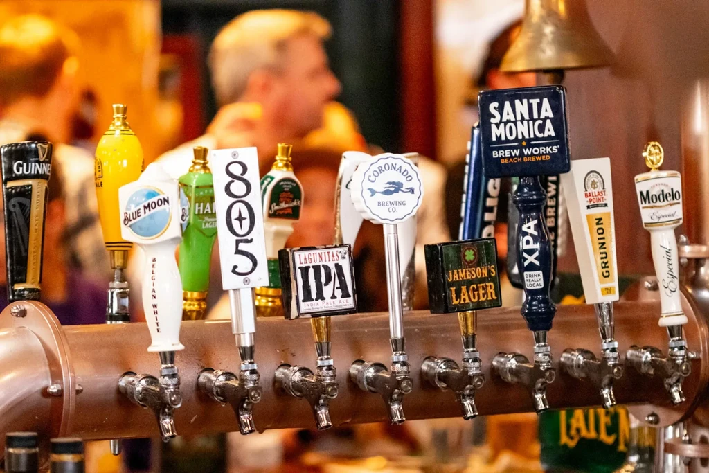 Row of bronze beer taps with various brand handles at a bar.