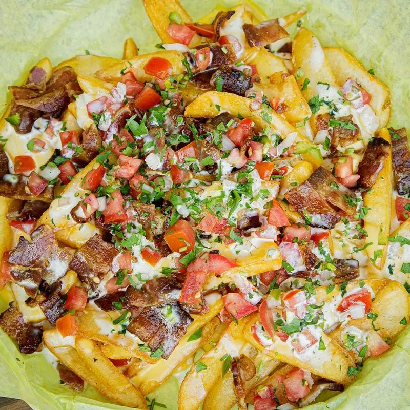 Loaded fries with melted cheese, bacon, creamy sauce, tomatoes, and herbs.
