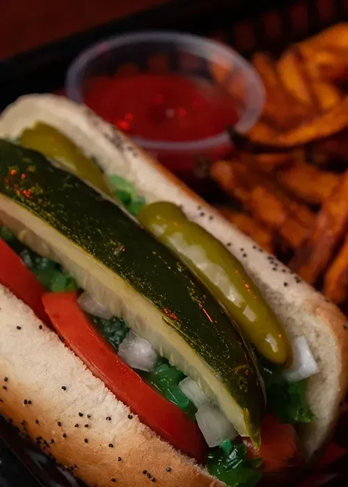 Hot dog in poppy seed bun, loaded with dill pickle, onions, tomatoes.