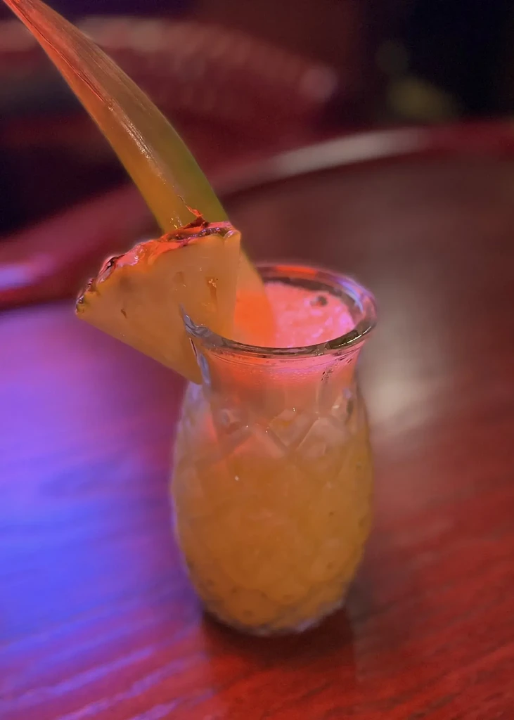 Tropical drink in a pineapple-shaped glass with pineapple garnish.